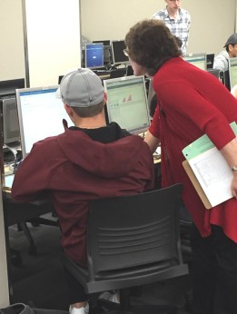A student sits in front of a computer as an instructor leans in to take a closer look at the monitor and provide help.